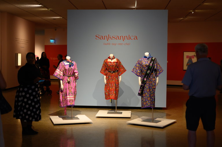 Three dresses by Lita Fontaine centred in a gallery filled with people.