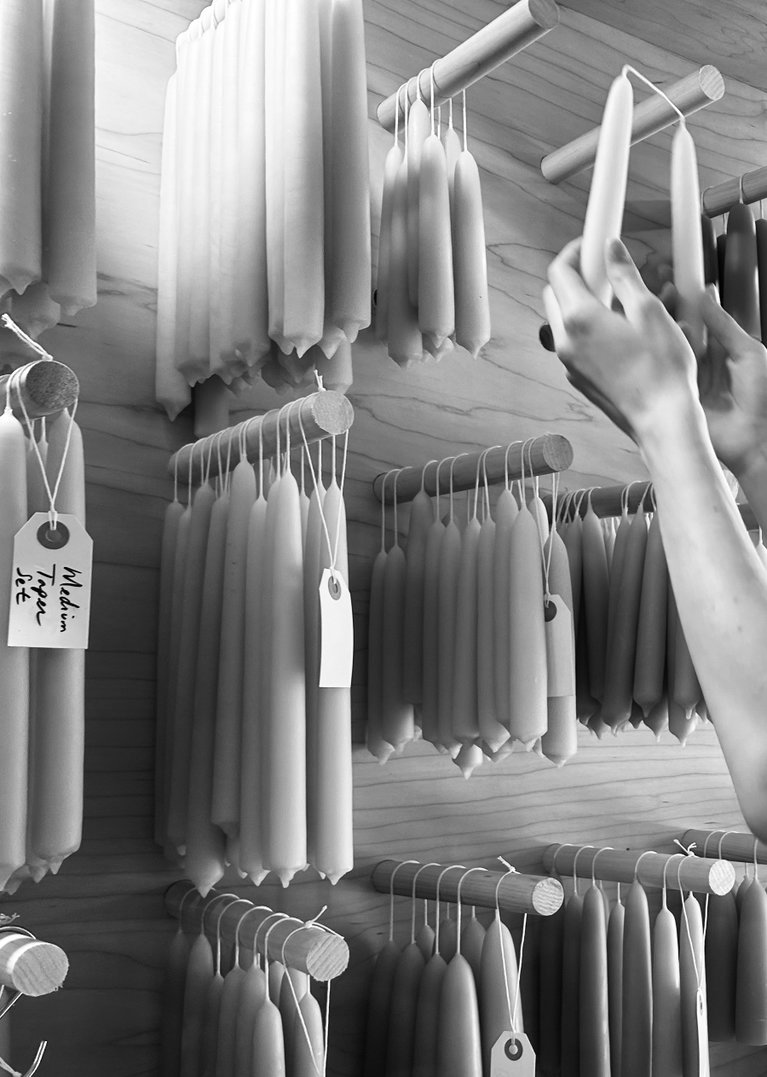 Image of a pair of hands reaching for a set of handdipped candle tapers, among rows of them hanging on a wall