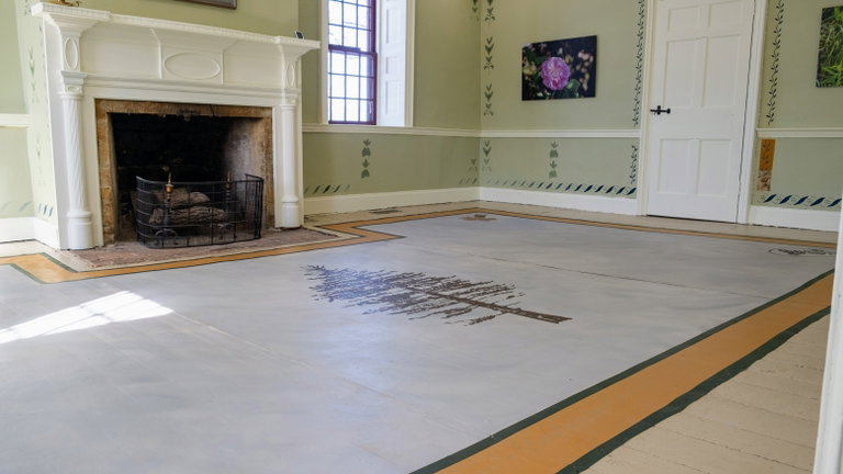 A painted floor covering stretches over the flooring of a room.