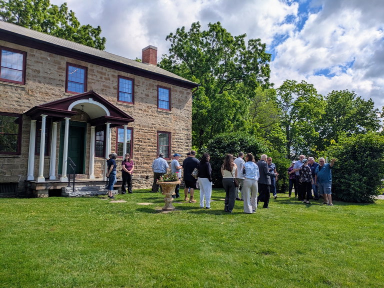 A group of people gather in front of a stone historic house.
