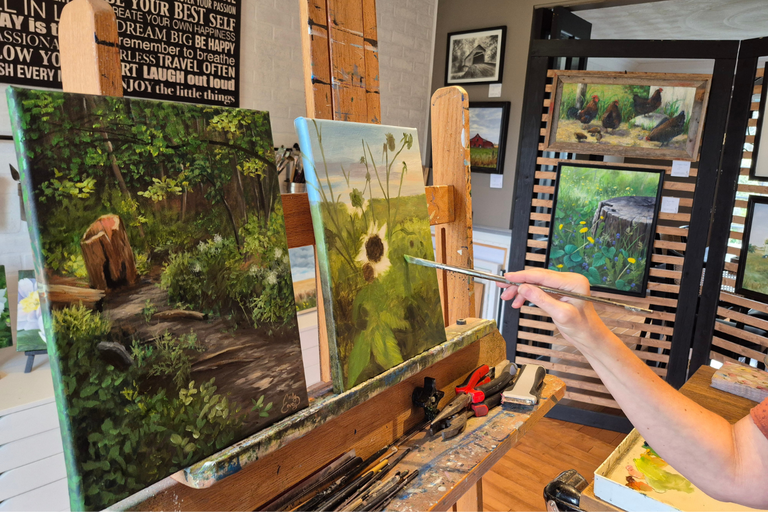 A close up of artist Carley Covey paints a landscape surrounded by lots of finished paintings her studio as part of Autumn In The Country arts fesitval