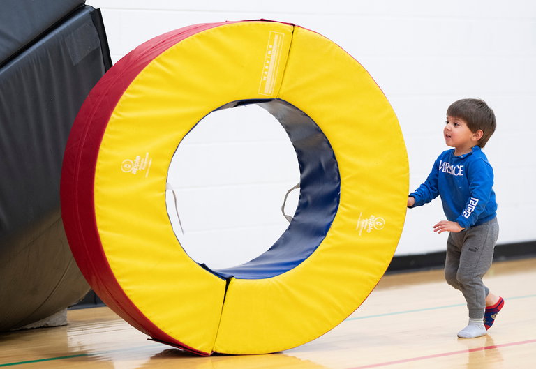 A child playing in the gym, pushing a foam tire.