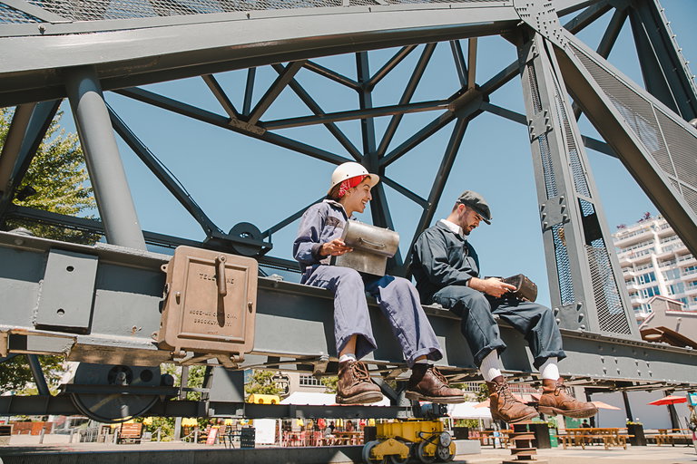 Two actors portraying The Shipyards Pals, sitting on the Burrard Dry Dock Crane.
