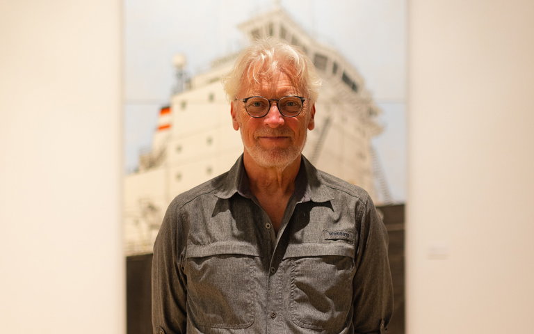 portrait of artist Peer Christensen standing in front a large painting of a steamship