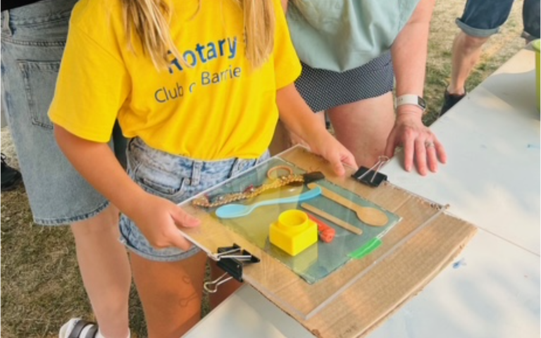A young person wearing a yellow shirt placing different types of objects found on the beach on cyanotype paper in preparation to place it out into the sun for exposure.