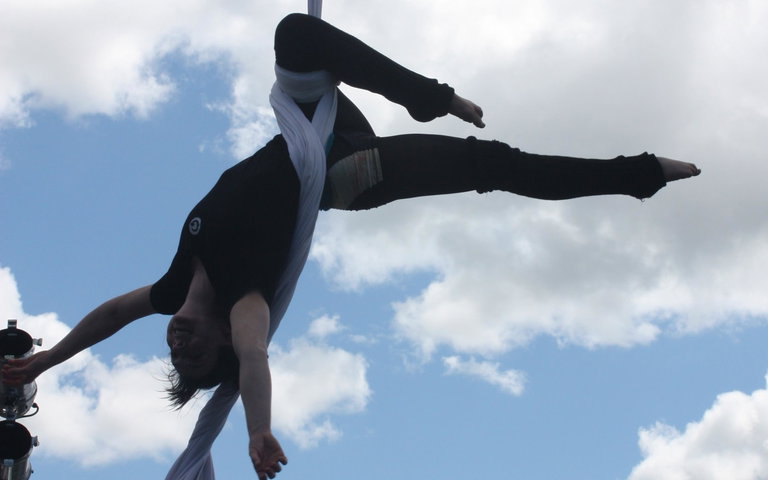 Woman hangs from areial silks outdoors