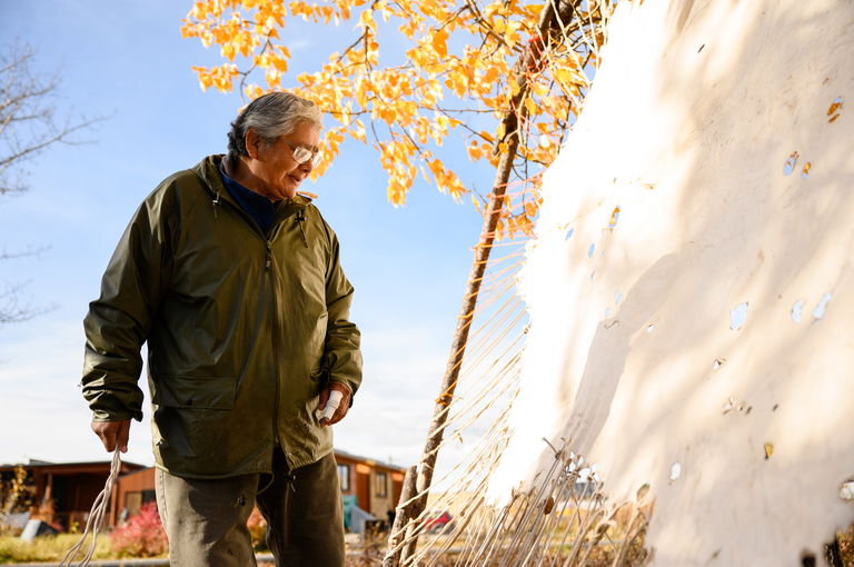 Elder Margaret Douville looks at a hide on a stretcher frame.