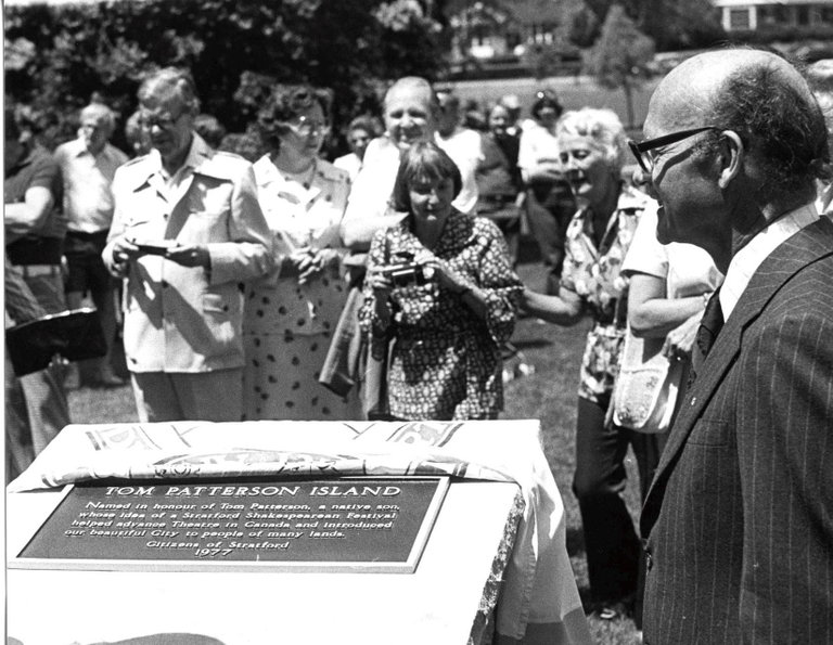 The dedication of Tom Patterson Island, 1977. Photo by Robert Ihrig/IhrigArt, courtesy of the Stratford - Perth Archives. Tom Patterson stands to the right of the island plaque surrounded by onlookers taking photos.