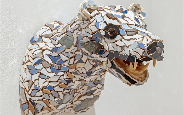 A mosaic of a bear head mounted on a white wall.
