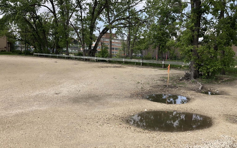 A photograph of a dirt field parking lot with puddles.