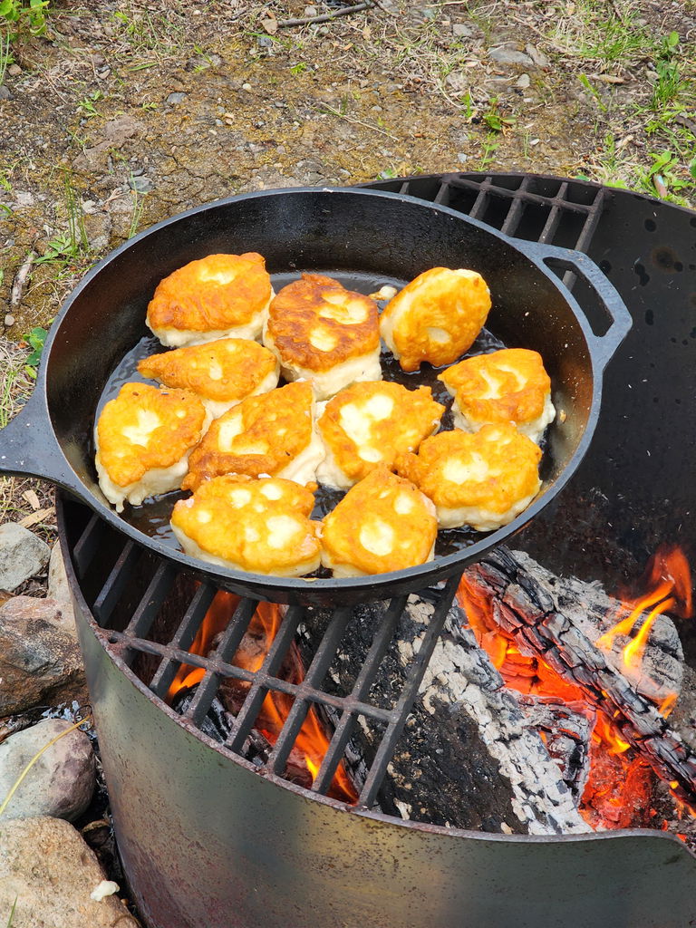 Image of bannock frying in a cast iron pan over a campfire