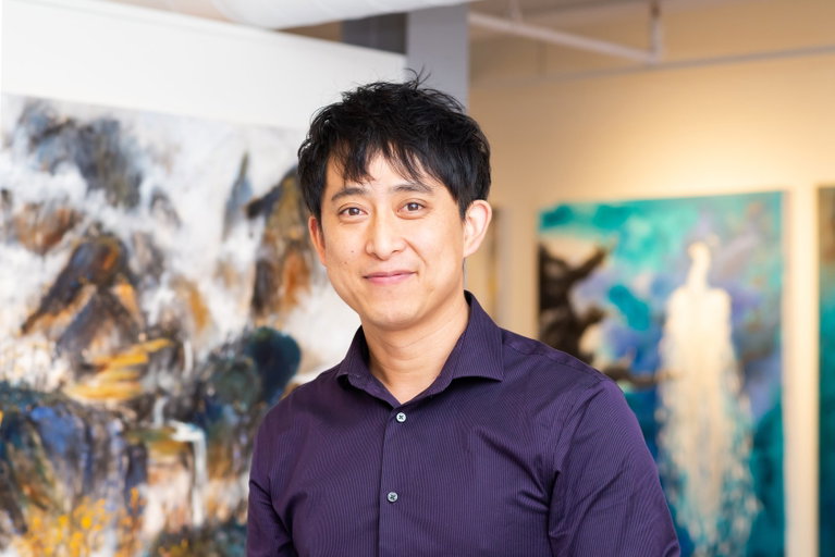 A man smiling in front of his paintings.