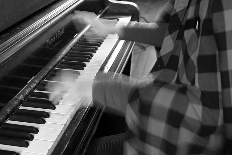 [ID: A black and white closeup photo of a person playing the piano. No face is shown and the hands are artistically blurry as the photo was taken during movent. End]