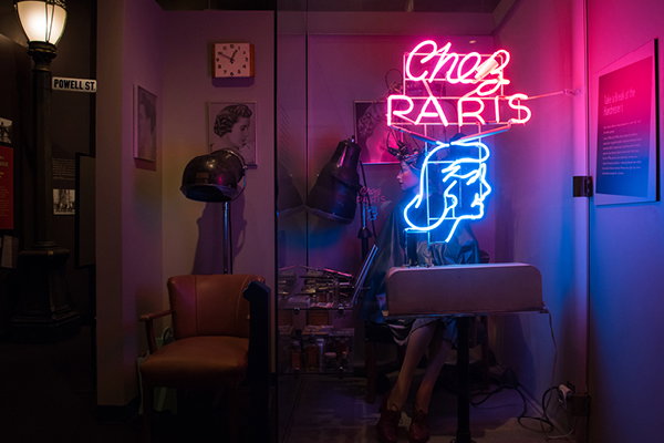 Chez Paris neon sign with a 1930s hair salon set up behind it, including a mannequin in the permanent wave machine and a hair dryer chair where guests can sit.