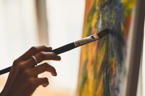 Close up of a hand holding a paintbrush adding strokes to a colourful canvas