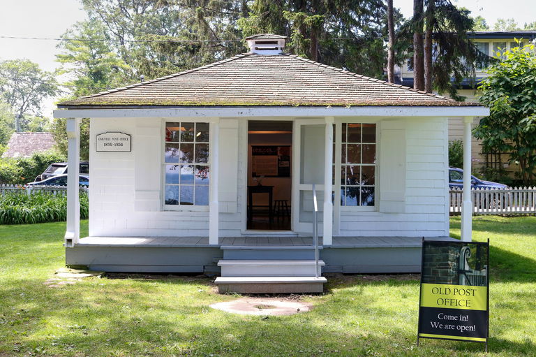 Small white wood building in a park setting. The front door is open to welcome visitors inside.