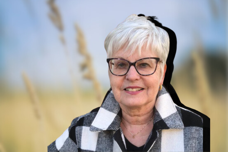 Helen Mourre smiles with round glasses, short white hair and a black and white checkered collared coat
