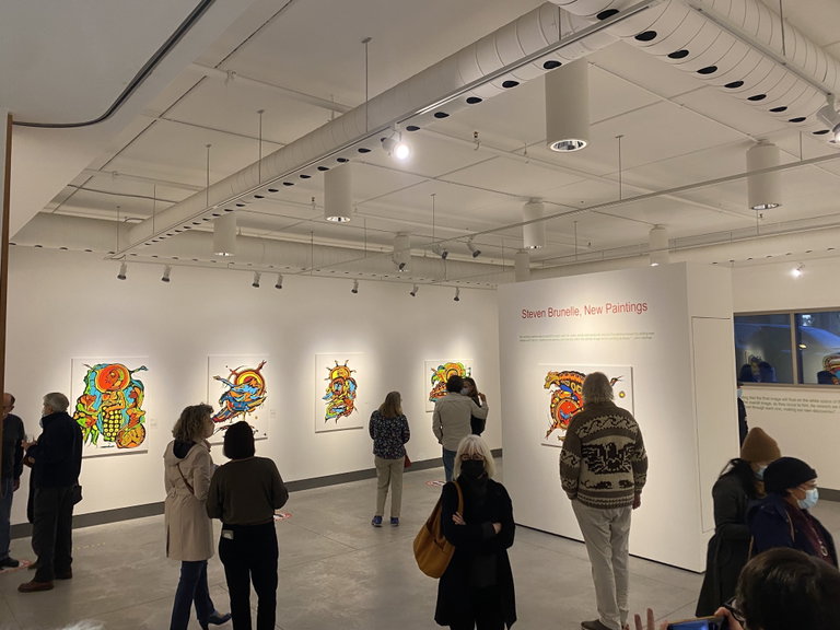 Visitors view colourful paintings displayed in a contemporary art gallery during an exhibition.