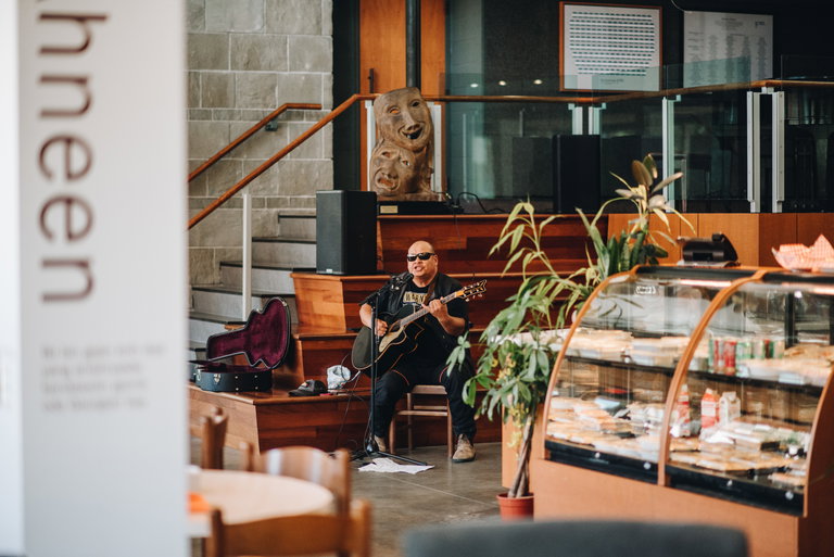 A man sitting down and playing guitar in a bright atrium