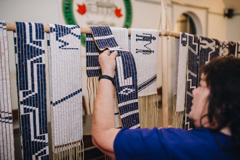 A person holding and looking at a dark blue Wampum Belt