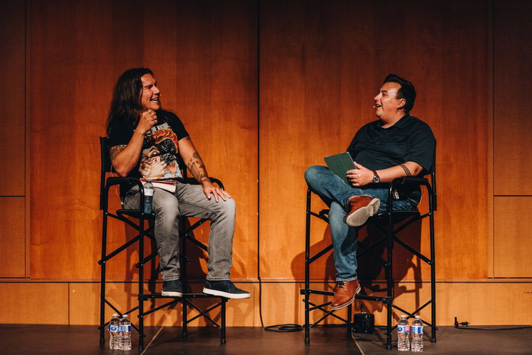 Two people sitting on stage having a conversation and laughing