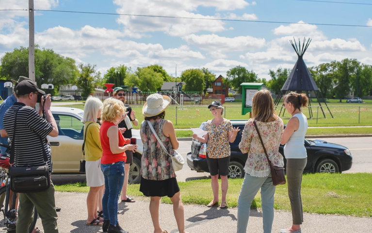 A group of people gather around a poet sharing their poem. It is a sunny, summery day with a blue sky.