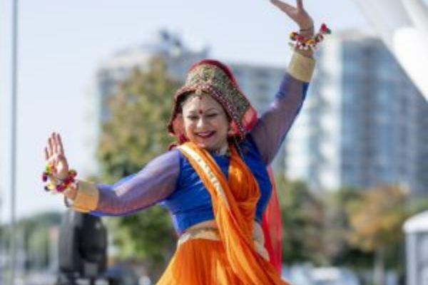 a woman wearing bright orange and blue clothing dances outside