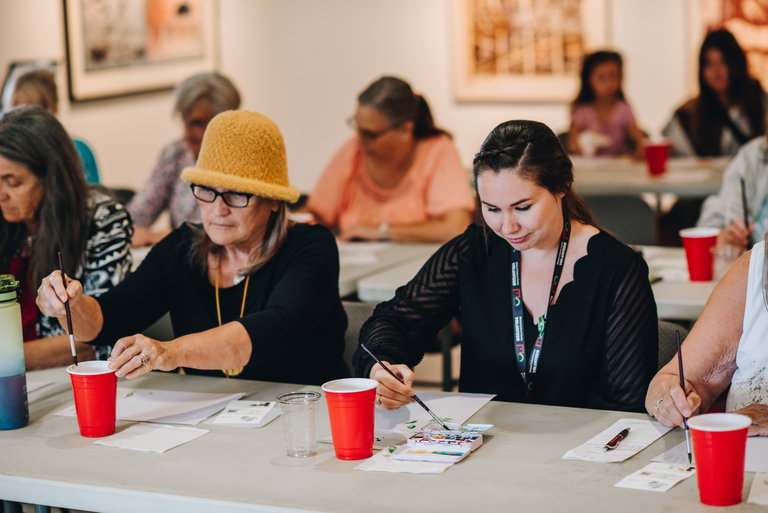 People sitting at tables in a gallery and painting with watercolours