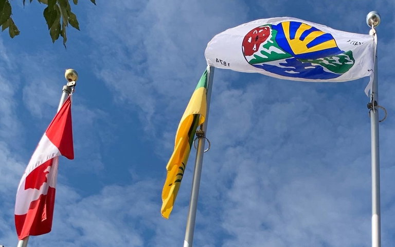 3 flags are shown.  On the left, the Canadian flag.  In the middle is the Saskatchewan flag.  On the right the Treaty 4 flag waves in the wind