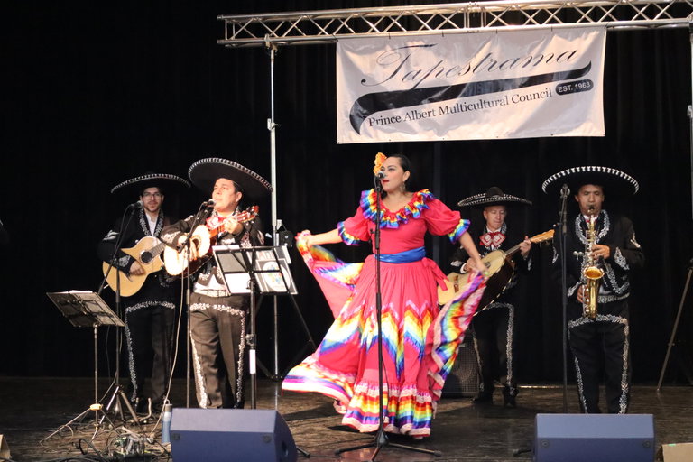 A mariachi band performs on stage with a colourfully dressed singer
