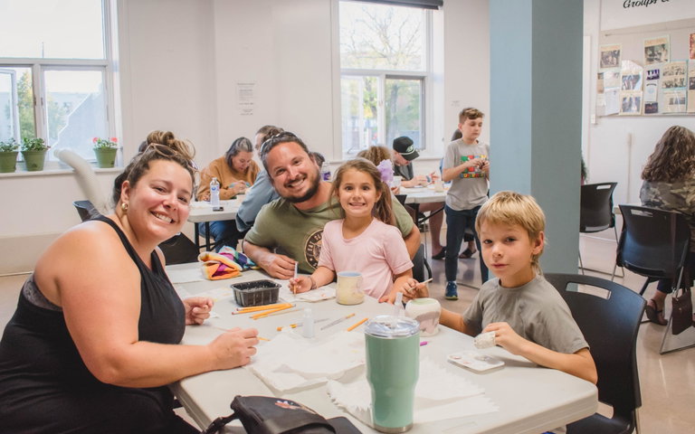 A family of four smile while painting pottery around a table.